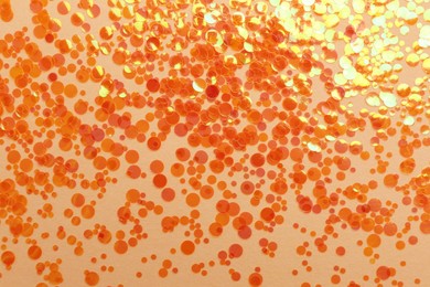 Photo of Shiny bright orange glitter on beige background, flat lay