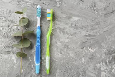 Different toothbrushes and eucalyptus branch on grey textured table, flat lay. Space for text