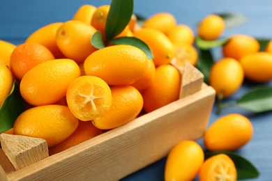 Photo of Fresh ripe kumquats in crate on blue wooden table, closeup