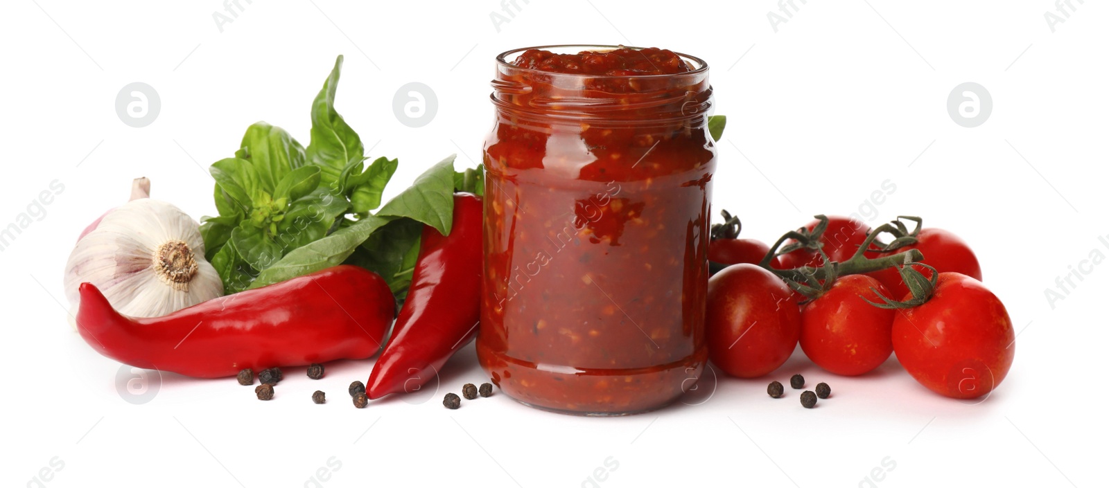 Photo of Glass jar of tasty adjika and ingredients on white background