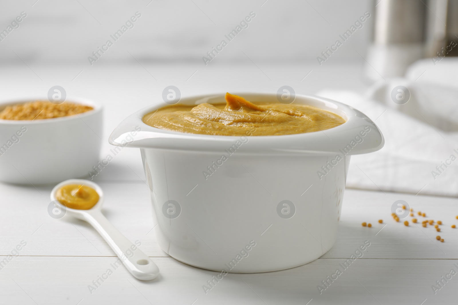 Photo of Tasty mustard sauce in bowl on white wooden table, closeup