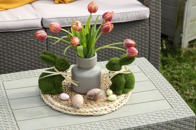 Photo of Terrace with Easter decorations. Bouquet of tulips in vase, bunny figures and decorated eggs on table outdoors