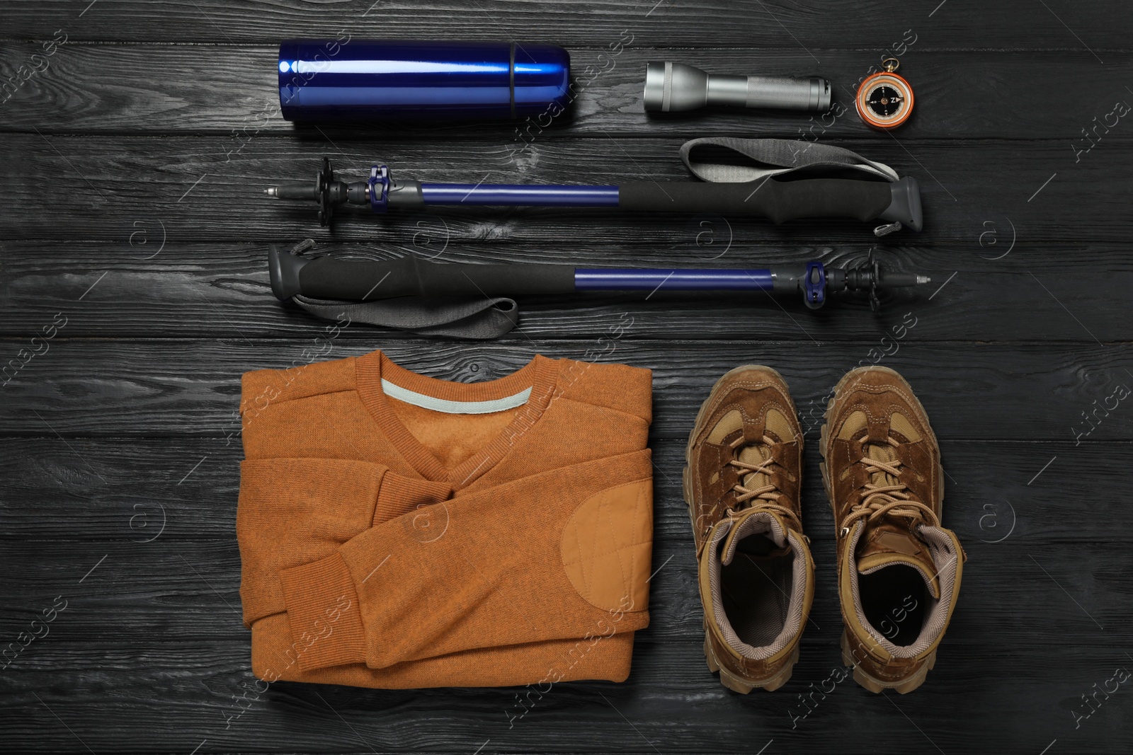 Photo of Flat lay composition with trekking poles and other hiking equipment on black wooden background
