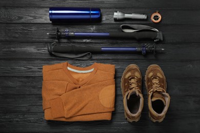 Photo of Flat lay composition with trekking poles and other hiking equipment on black wooden background