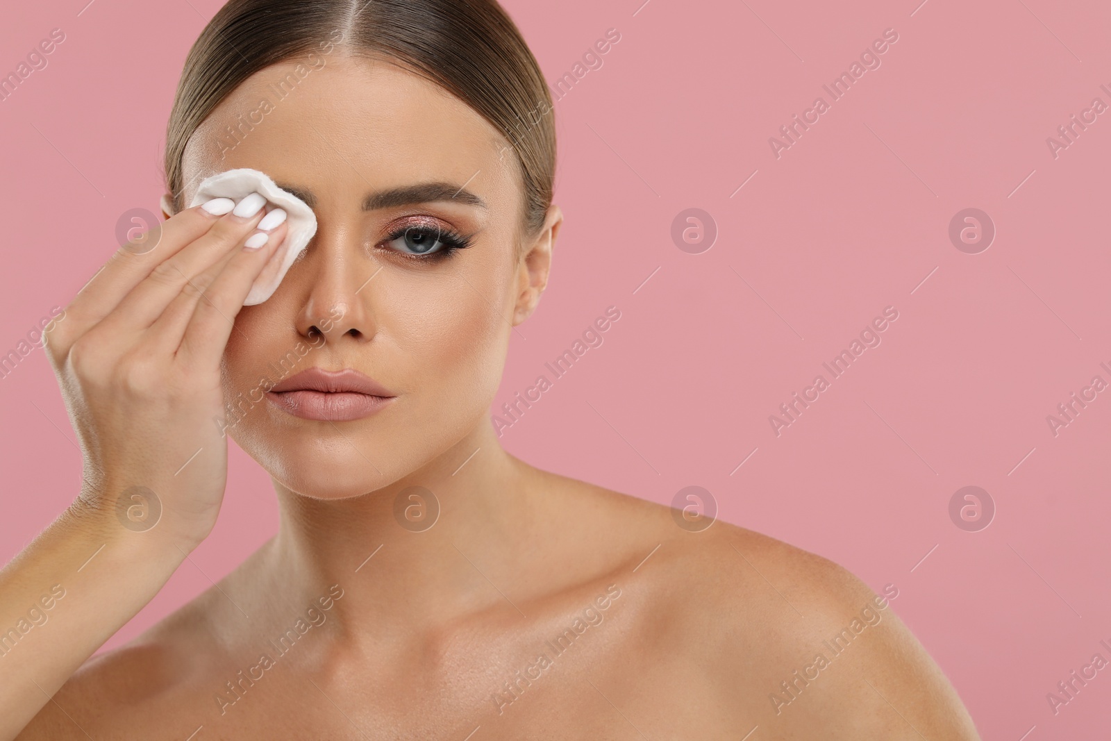 Photo of Beautiful woman removing makeup with cotton pad on pink background, space for text