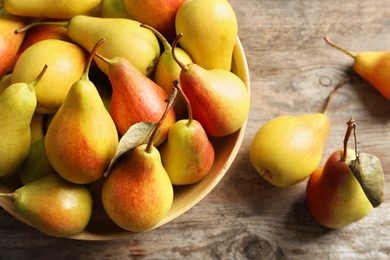 Photo of Bowl with ripe pears on wooden background, top view