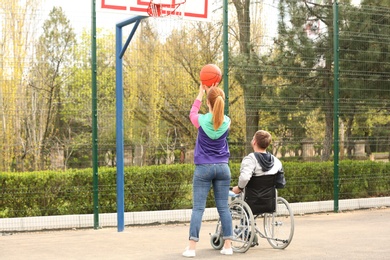Photo of Man in wheelchair and young woman playing basketball on sports ground