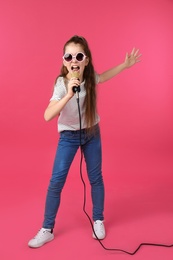 Cute girl singing in microphone on color background