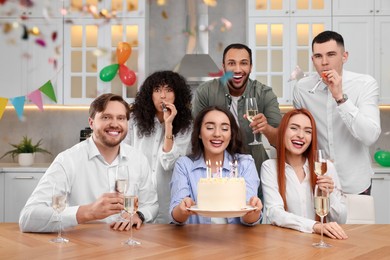 Happy friends with tasty cake celebrating birthday in kitchen