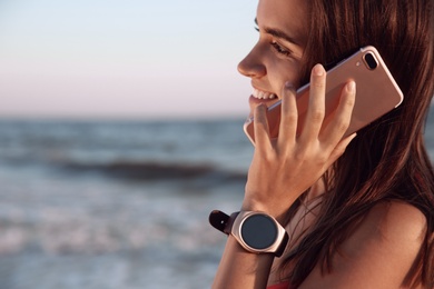 Photo of Young woman with smart watch talking on phone at beach, closeup