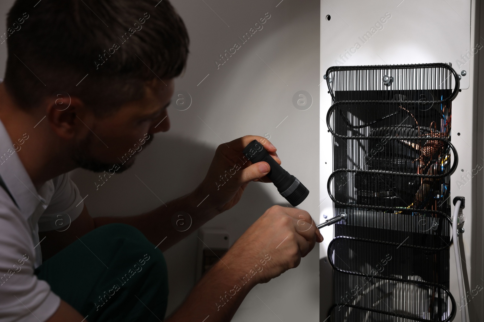 Photo of Professional electrician with flashlight fixing refrigerator indoors