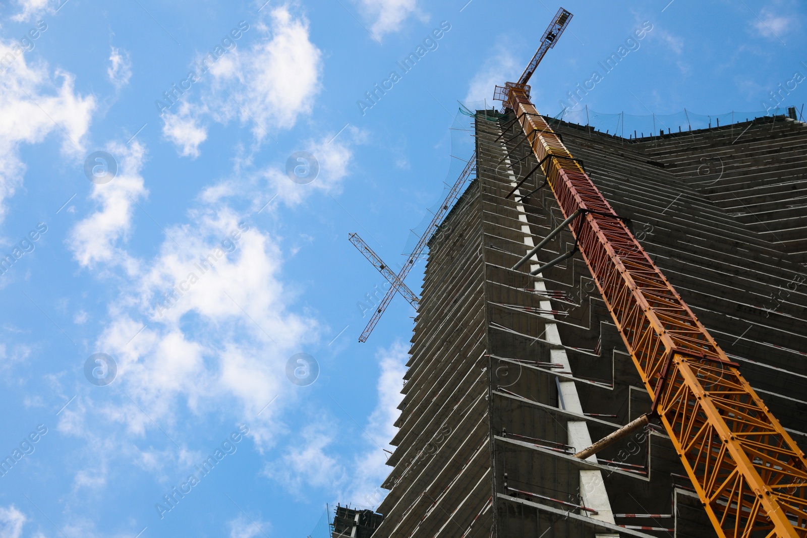 Photo of Construction site with tower crane near unfinished building under cloudy sky, low angle view