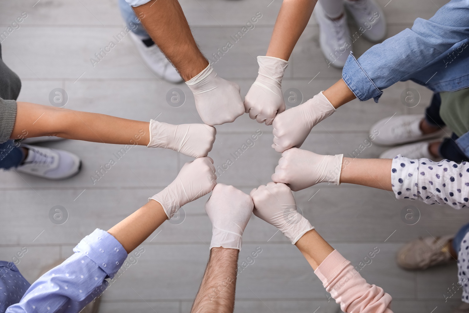 Photo of People in white medical gloves joining fists indoors, top view