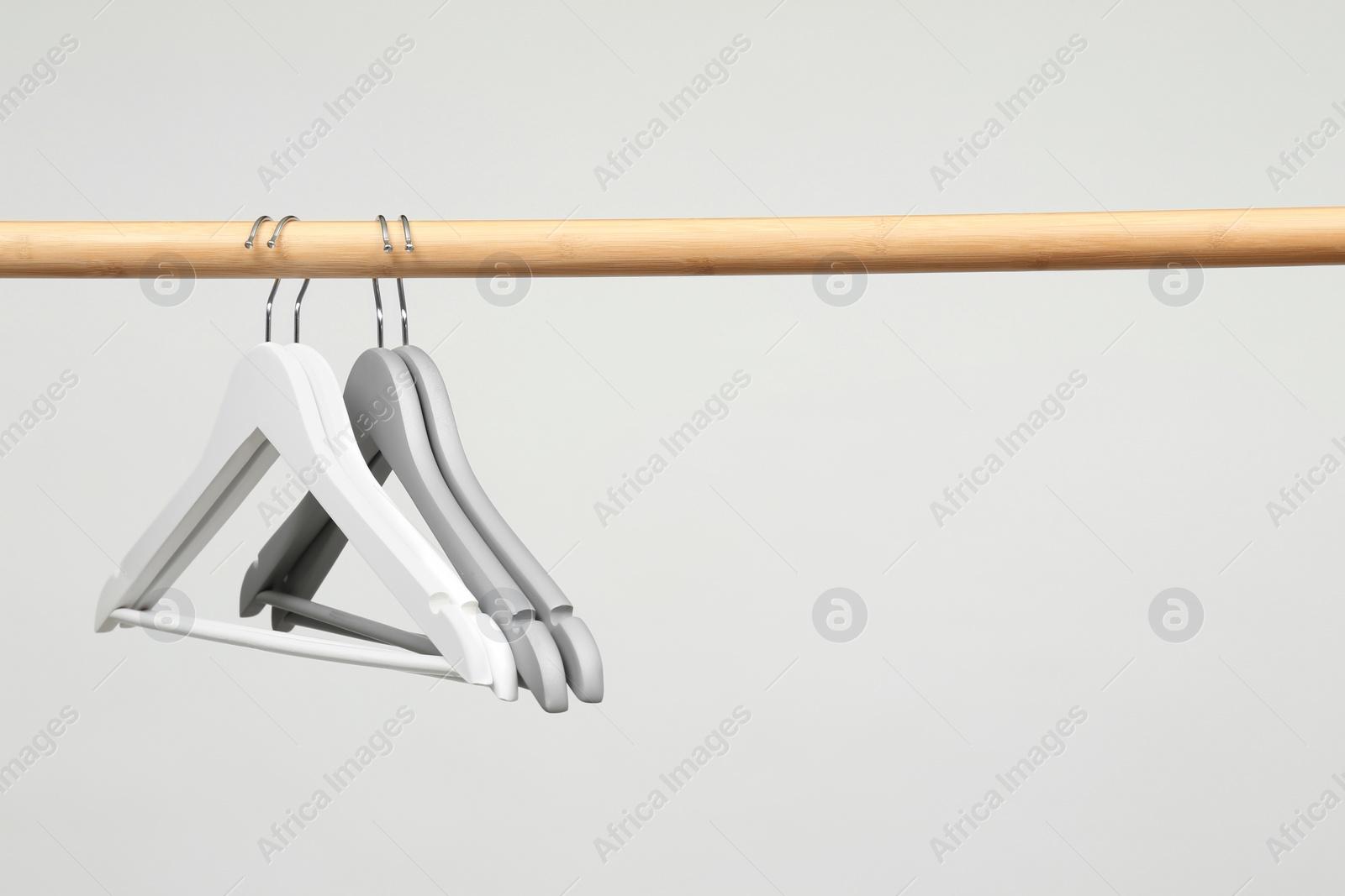 Photo of Empty clothes hangers on wooden rail against light background. Space for text