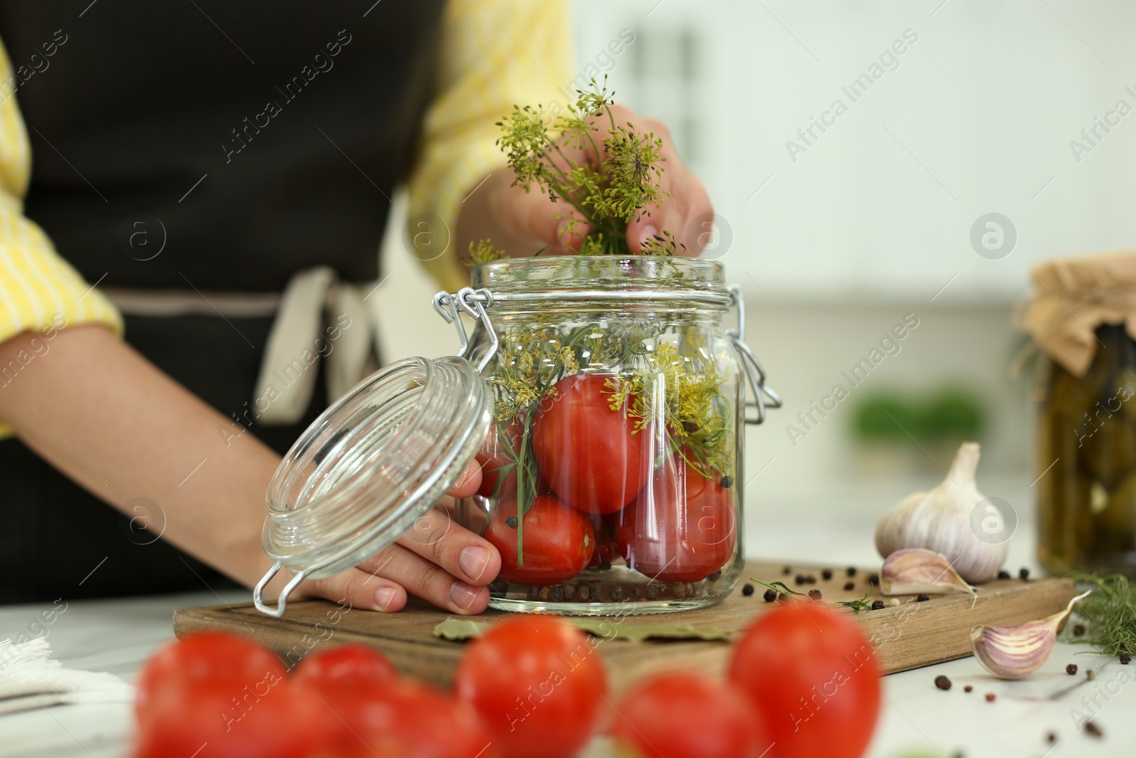 Photo of Woman putting dill into pickling jar at table in kitchen, closeup