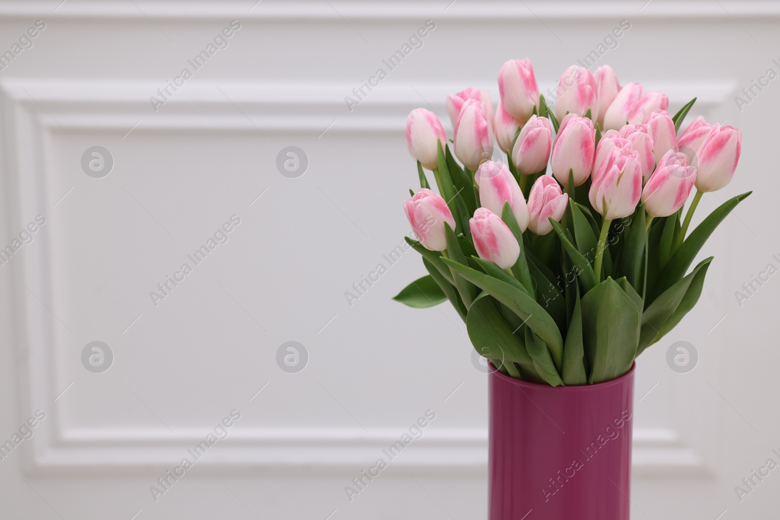 Photo of Beautiful bouquet of fresh pink tulips near white wall. Space for text