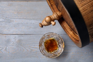 Photo of Barrel with tap and glass of tasty whiskey on light gray wooden table, flat lay. Space for text