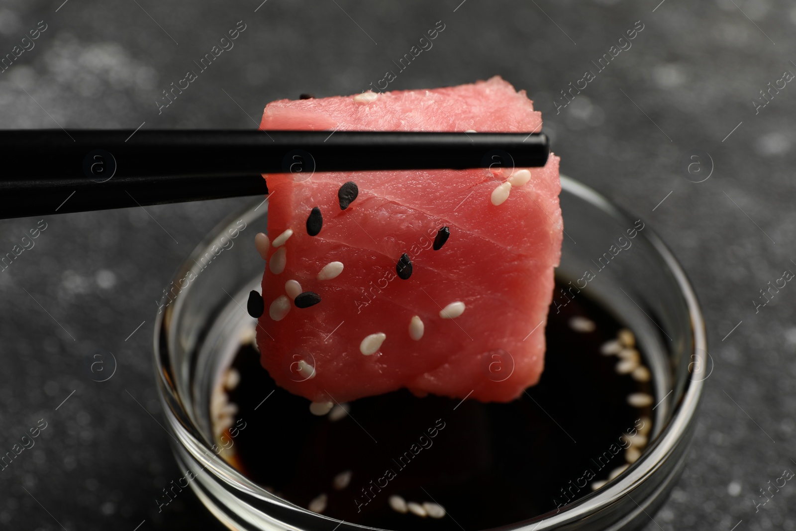 Photo of Dipping tasty sashimi (piece of fresh raw tuna) into soy sauce at black table, closeup