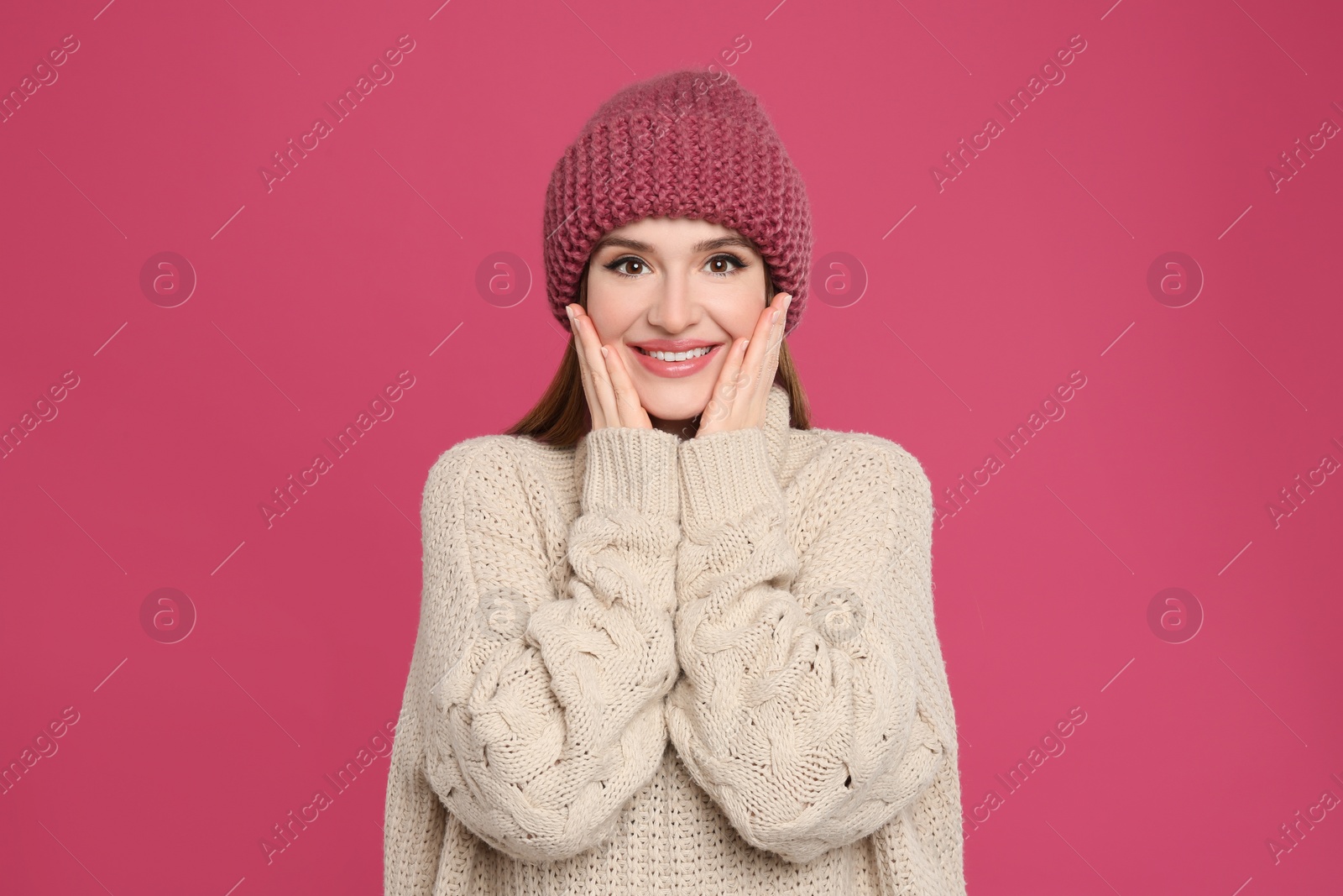 Photo of Young woman wearing warm sweater and hat on crimson background. Winter season