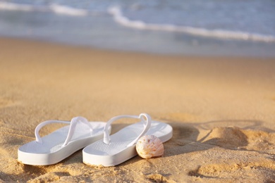 Photo of White flip flops and shell on sand near sea, space for text. Beach accessories