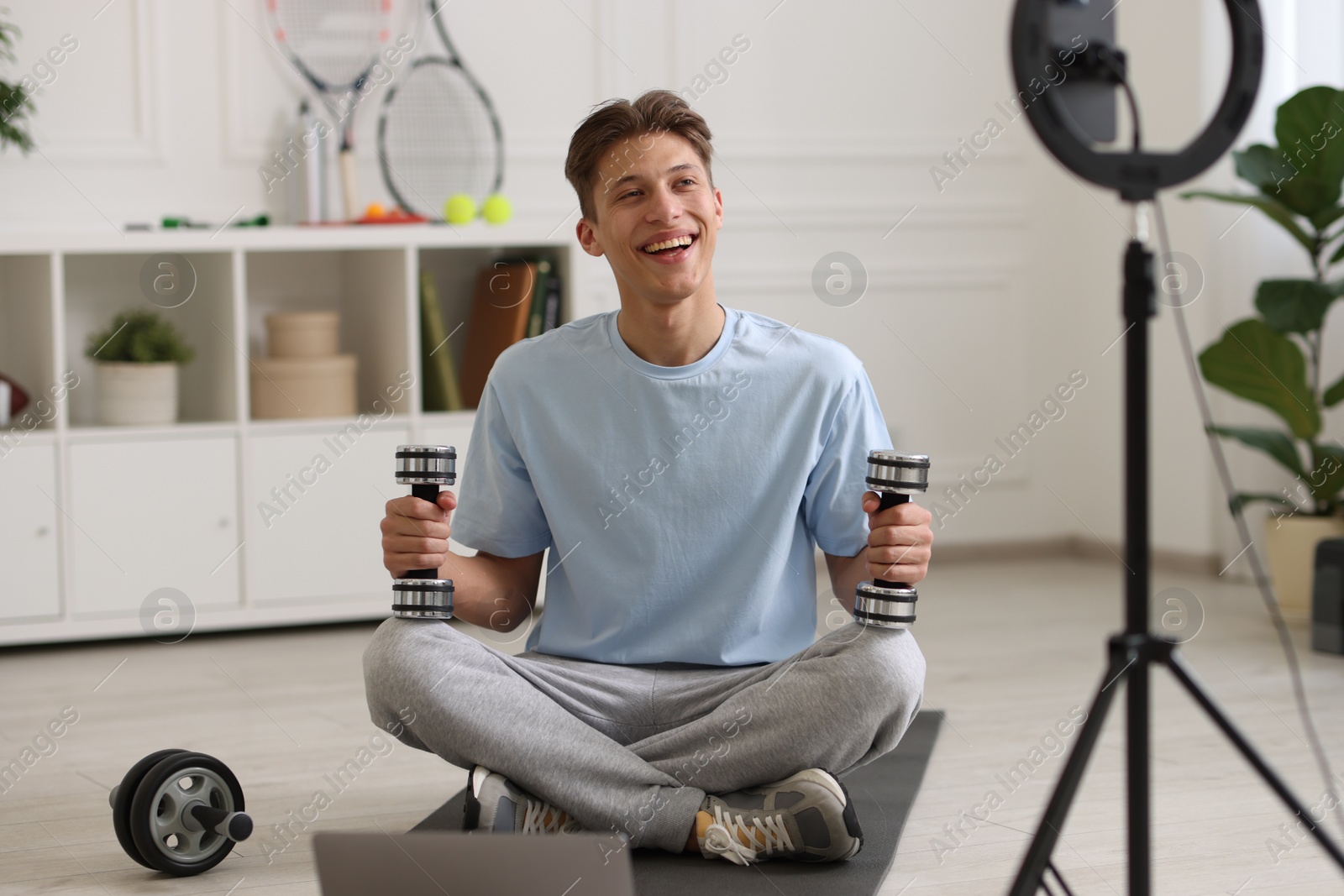 Photo of Smiling sports blogger holding dumbbells while streaming online fitness lesson at home