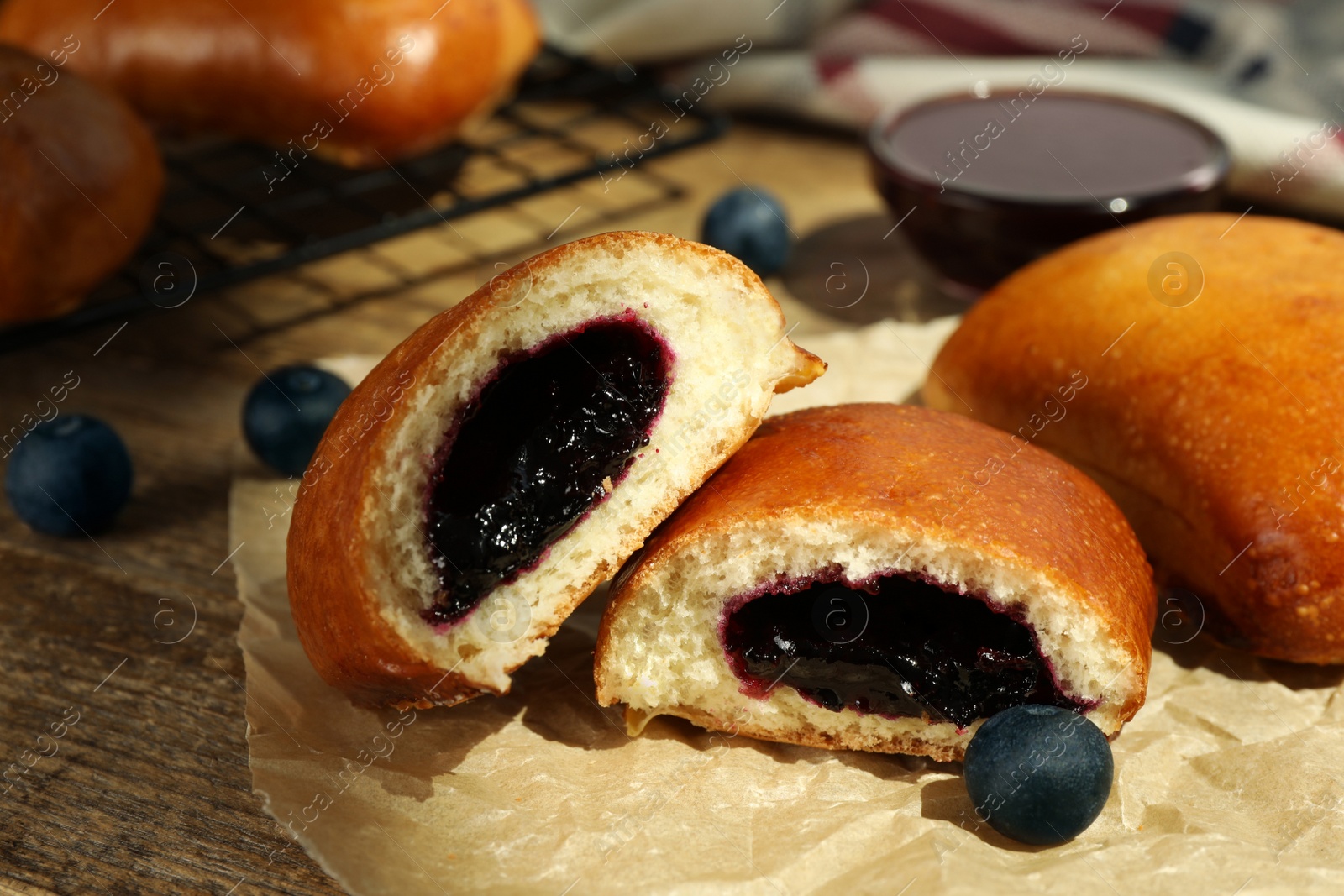 Photo of Delicious baked patties with jam and blueberries on wooden table, closeup