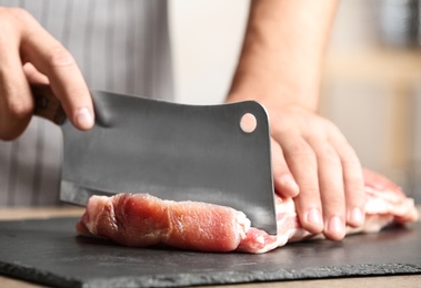 Photo of Man cutting fresh raw meat on table in kitchen, closeup
