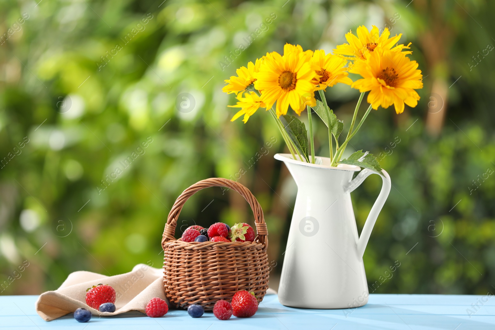 Photo of Wicker basket with different fresh ripe berries and beautiful flowers on light blue table outdoors