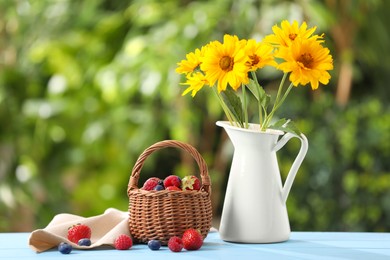 Photo of Wicker basket with different fresh ripe berries and beautiful flowers on light blue table outdoors