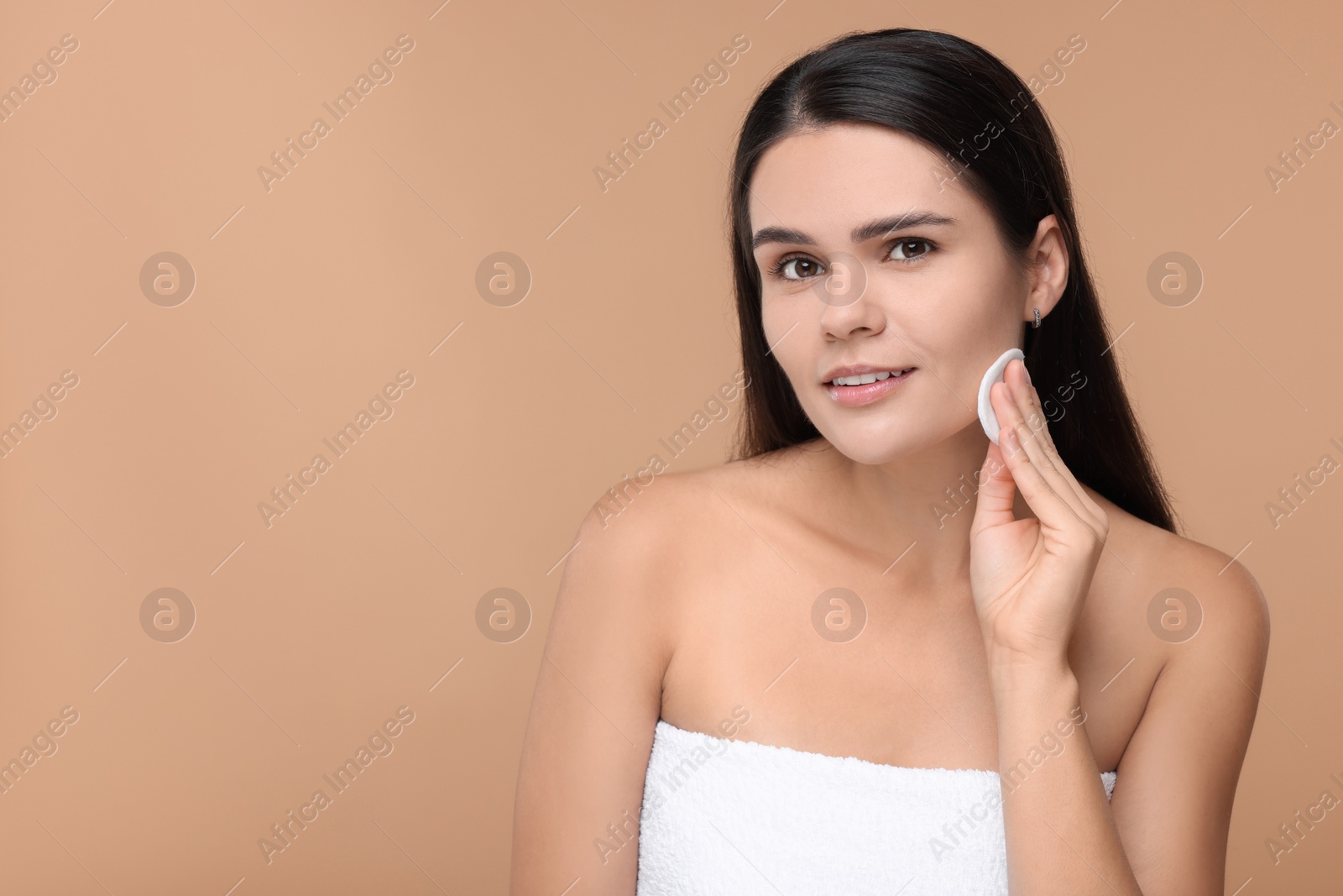 Photo of Young woman cleaning her face with cotton pad on beige background. Space for text