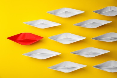 Photo of Group of paper boats following red one on yellow background, flat lay. Leadership concept