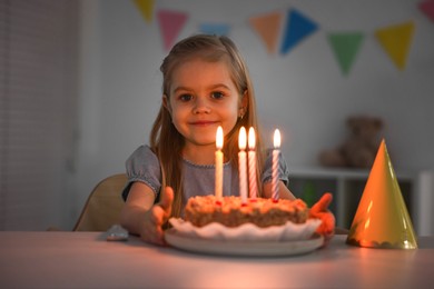 Photo of Cute girl with birthday cake at table indoors