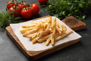 Photo of Delicious French fries with cheese sauce, tomatoes and dill on black table