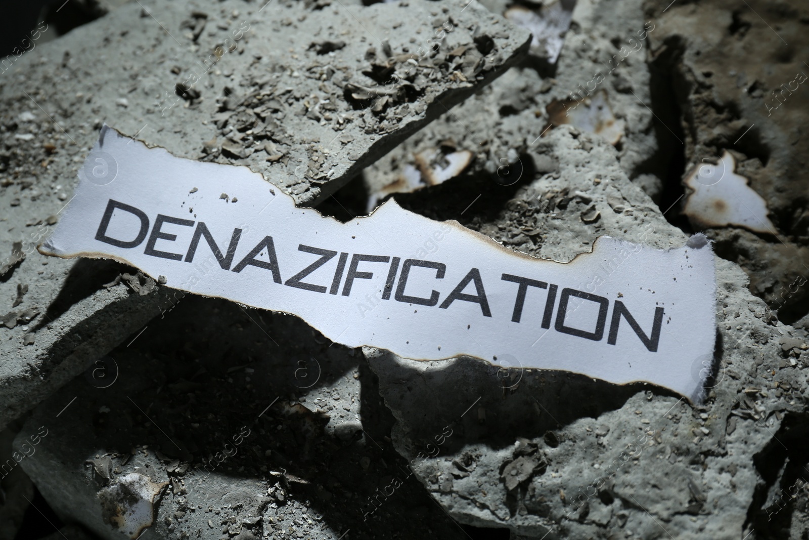 Photo of Paper with word Denazification on pieces of concrete, closeup