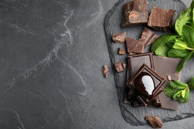 Photo of Tasty chocolate pieces with syrup and mint on black table, flat lay. Space for text