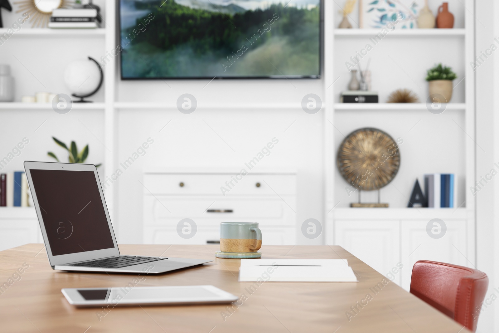 Photo of Interior design. Cosy workplace with laptop, tablet and cup on wooden table near tv area. Space for text