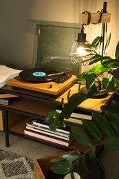 Stylish turntable with vinyl record on tv table in cozy room