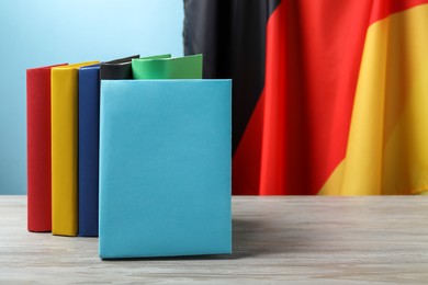 Learning foreign language. Different books on wooden table near flag of Germany, space for text