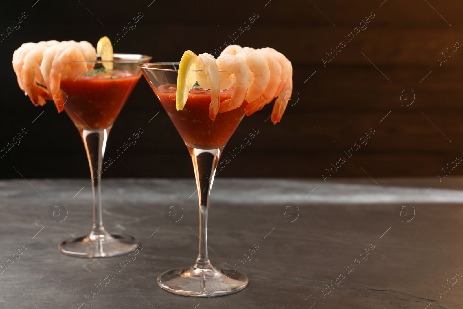 Photo of Tasty shrimp cocktail with sauce in glasses and lemon on grey table, space for text