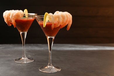 Tasty shrimp cocktail with sauce in glasses and lemon on grey table, space for text