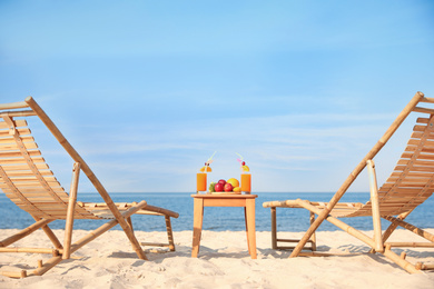 Photo of Wooden deck chairs near table with fruits and drinks on beach