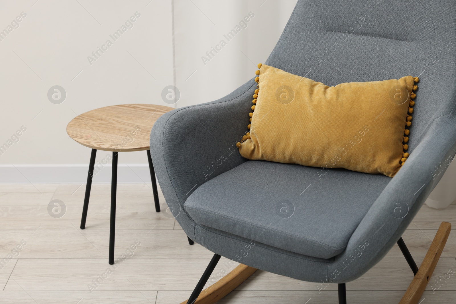 Photo of Soft pillow on rocking armchair and side table indoors