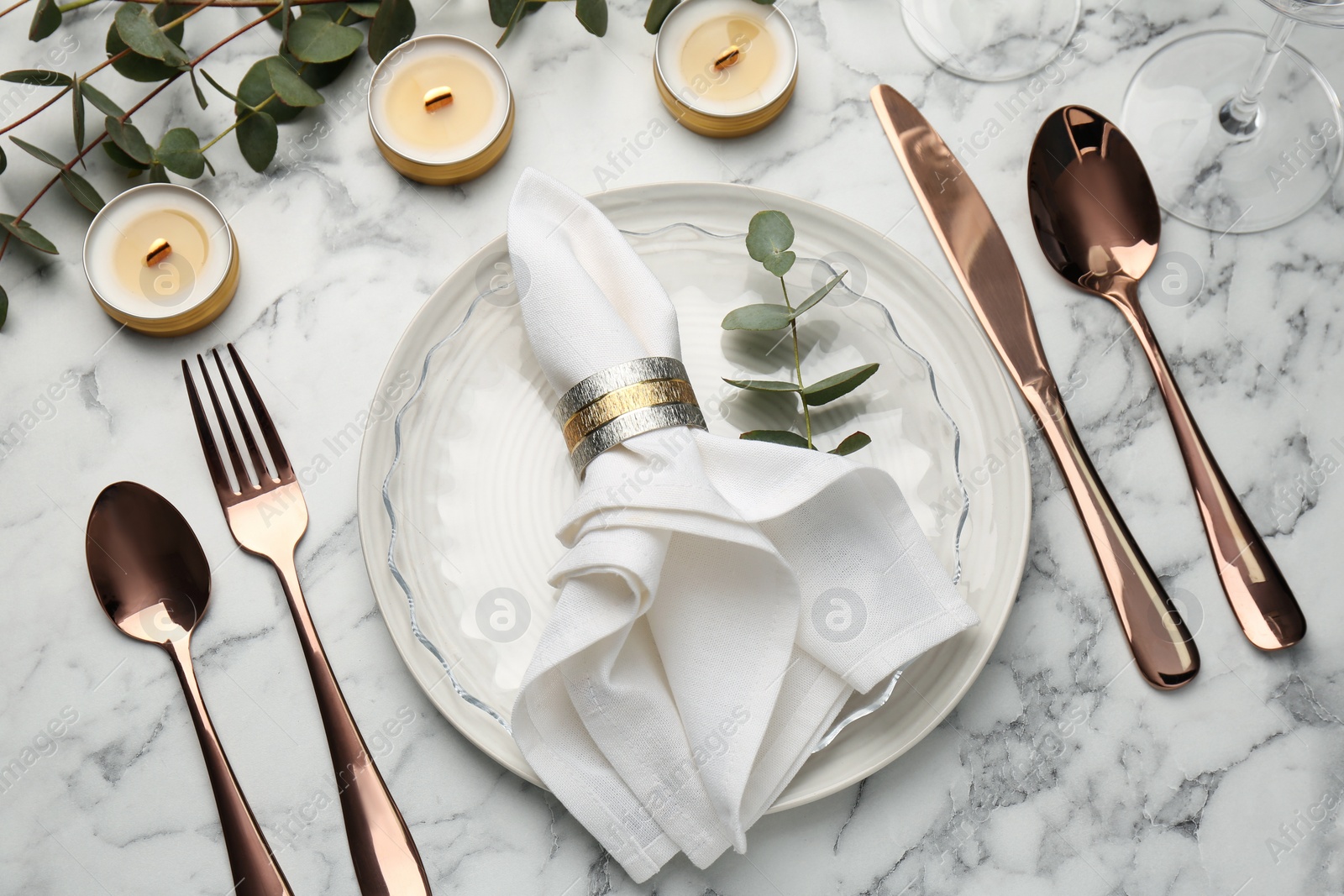 Photo of Beautiful place setting with candles and eucalyptus on white marble table, above view