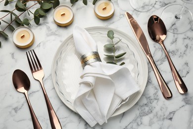 Beautiful place setting with candles and eucalyptus on white marble table, above view
