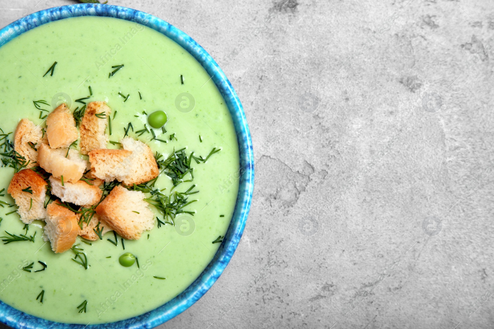 Photo of Green pea soup with croutons in bowl on grey background, top view