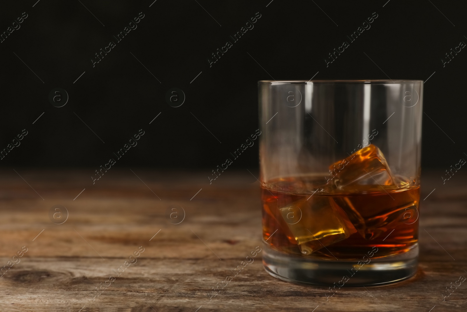Photo of Golden whiskey in glass with ice cubes on table. Space for text