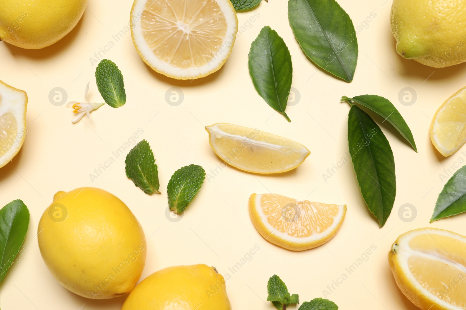 Photo of Many fresh ripe lemons with green leaves and flower on beige background, flat lay