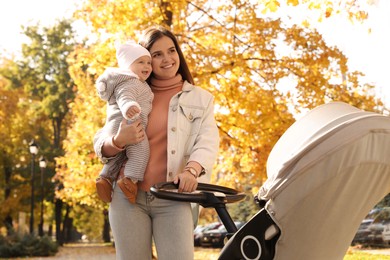 Happy mother walking with her baby daughter and stroller outdoors on sunny autumn day