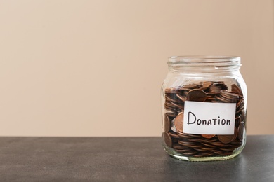 Donation jar with coins on table  against color background. Space for text