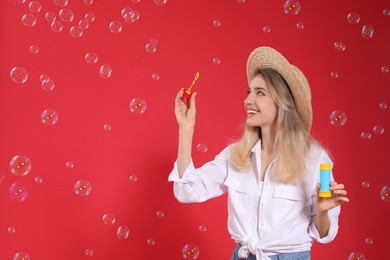 Photo of Young woman blowing soap bubbles on red background, space for text